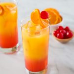 A glass of orange juice next to a bowl of cherries