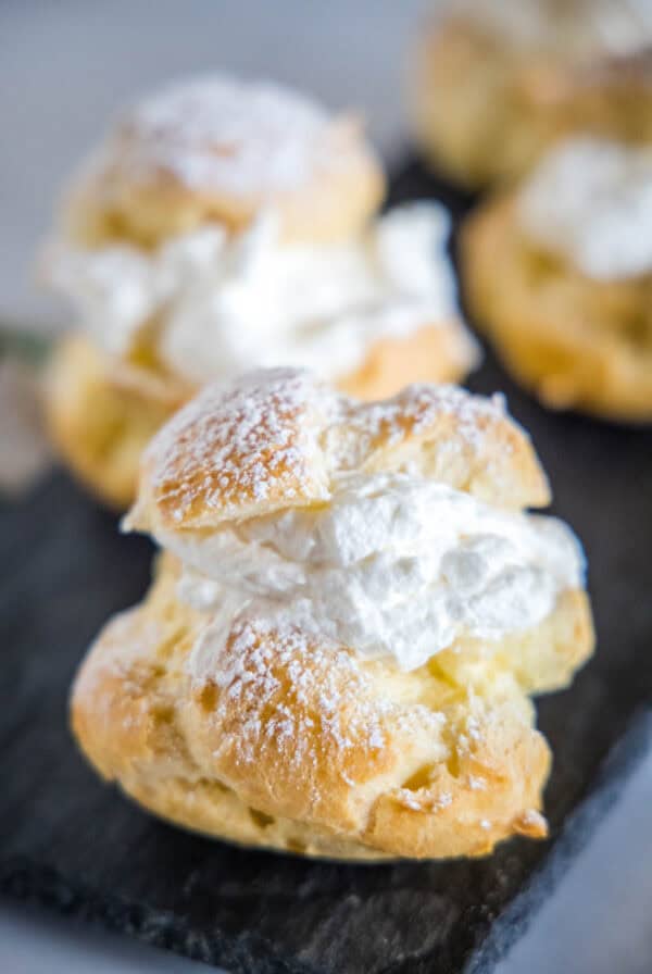 Close up of a cream puff dusted with powdered sugar on a platter with more cream puffs in the background.