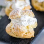 Close up of a cream puff dusted with powdered sugar on a platter with more cream puffs in the background.