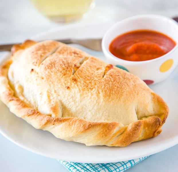 A plate with a calzone and marinara sauce, with Calzone