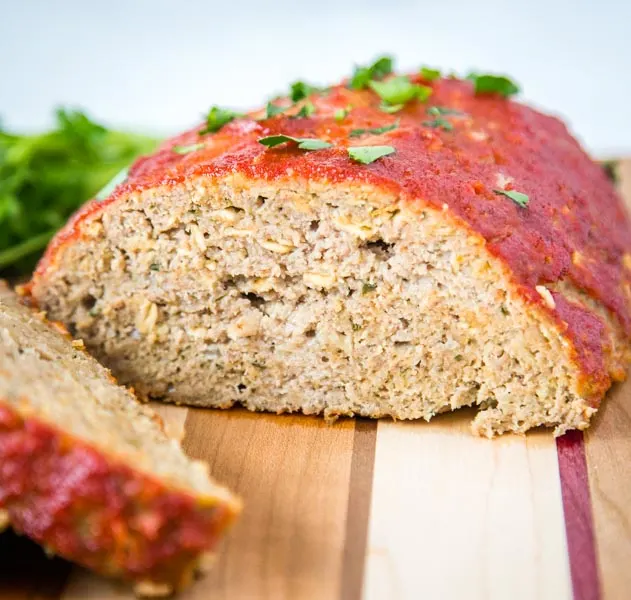 A slice of meatloaf sitting on top of a wooden cutting board, with Dinner and Meatloaf