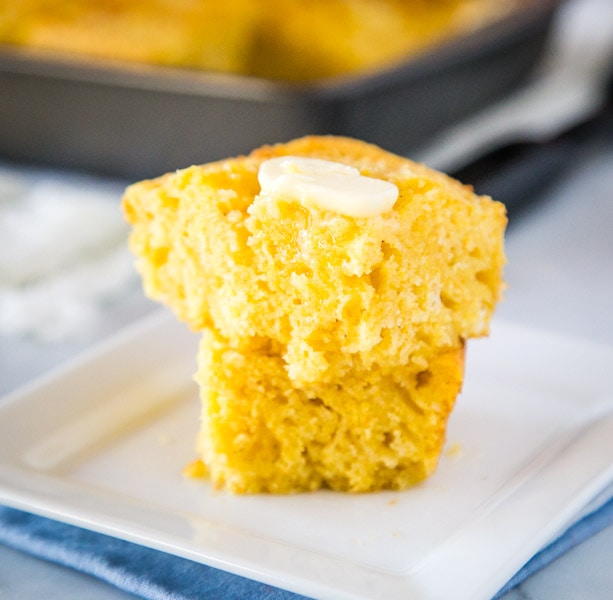 A piece of cornbread with butter on a plate, with Bread and Cornbread