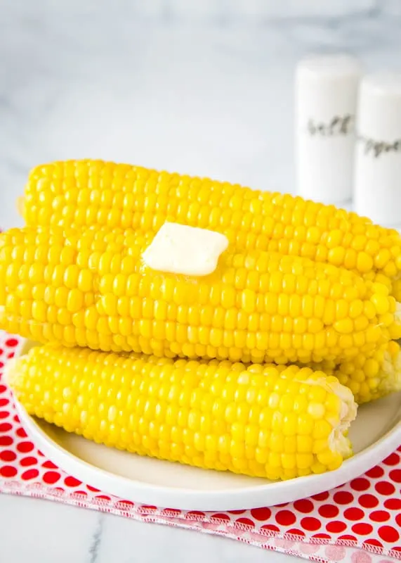pressure cooker corn on the cob stacked on a white plate with pat of butter on top