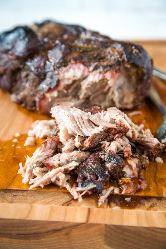 Smoked pork butt on cutting board with pile of pulled pork out front