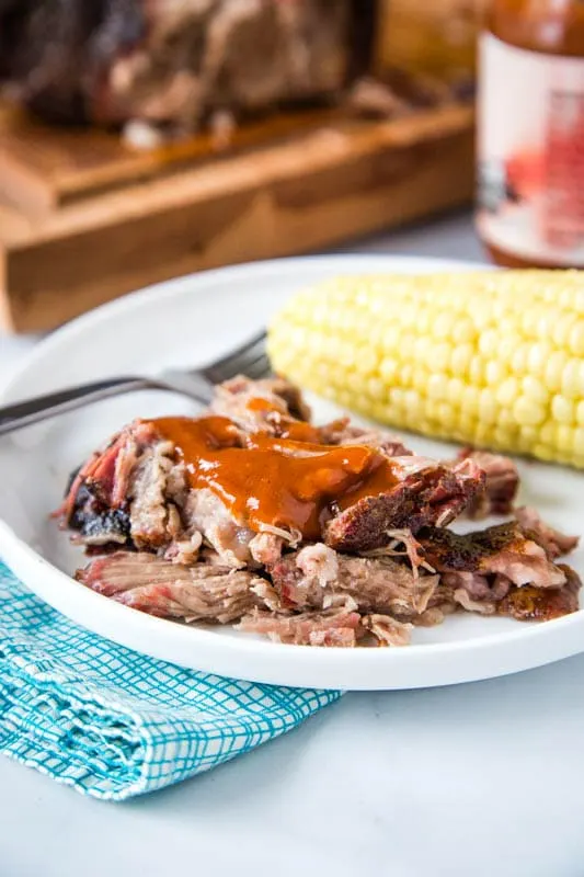 smoked pulled pork with bbq sauce on plate with corn on the cob