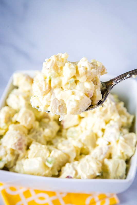 spoonful of homemade potato salad over a white bowl of potatoes