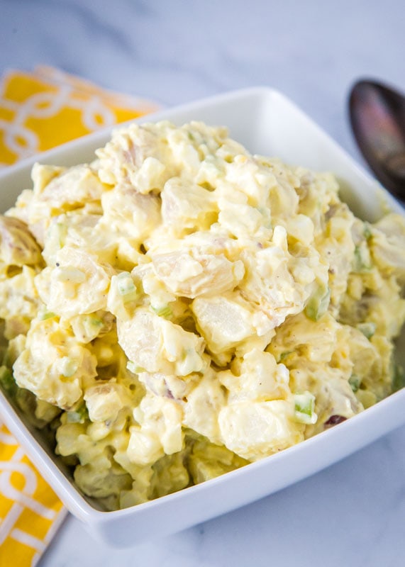 Old fashioned potato salad in white bowl with yellow napkin