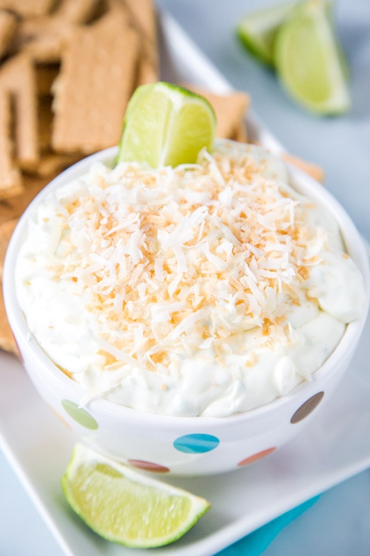 coconut lime cheesecake dip in bowl with lime wedge and toasted coconut on top
