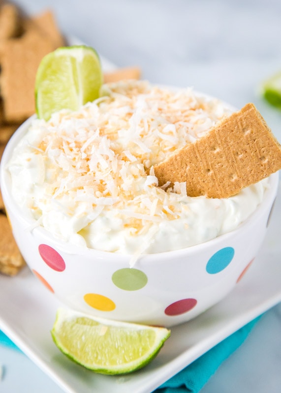 Cheesecake dip with toasted coconut and lime wedge in bowl with graham crackers