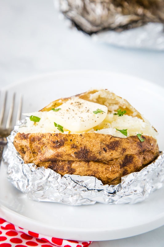 baked potato in foil on white plate cut open with butter