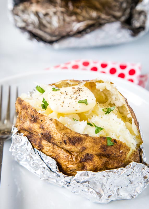grilled baked potato on white plate with butter and chives