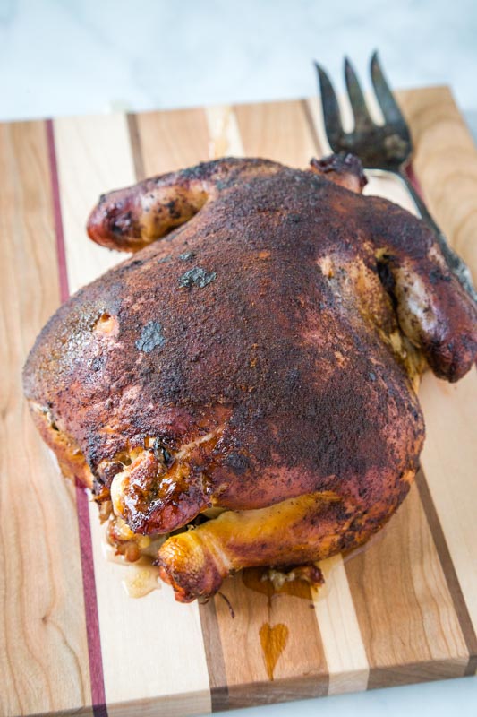 whole smoked chicken on cutting board with a fork