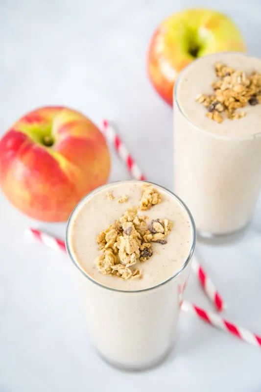 apple smoothie in a glass with an apple and straw next to it