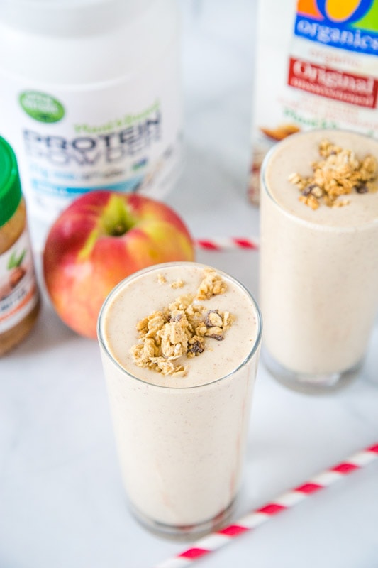 apple smoothie in a glass with milk, apple, protein powder and almond butter in background