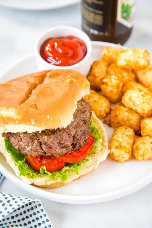 hamburger on bun with tater tots on a plate