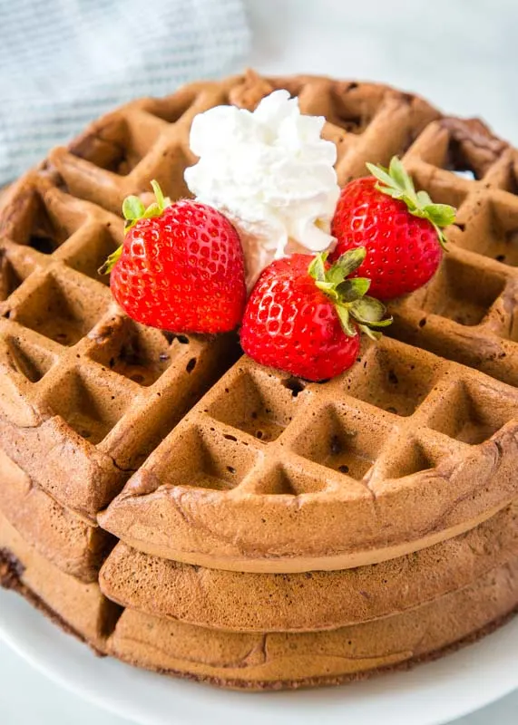 chocolate waffle on plate with whipped cream and strawberries