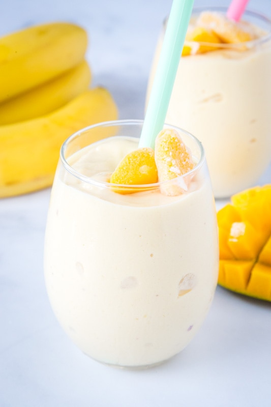 mango smoothie in a glass with sliced mango next to it
