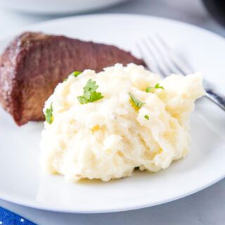 cropped mashed potatoes on a white plate with steak