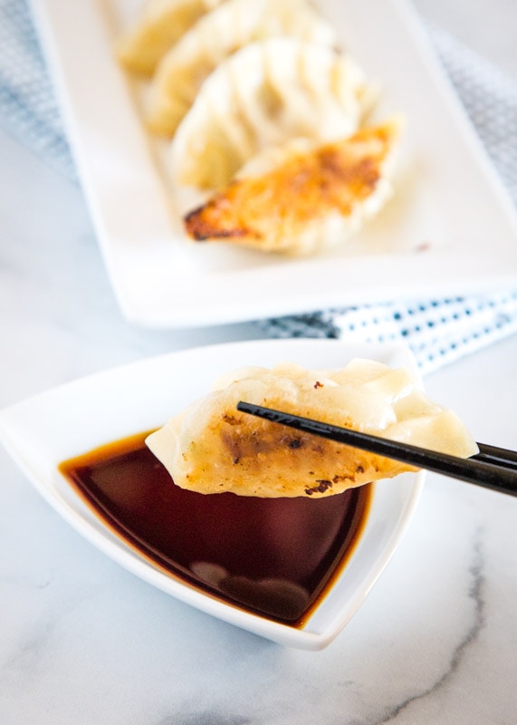 chopsticks holding potsticker to dip in soy sauce