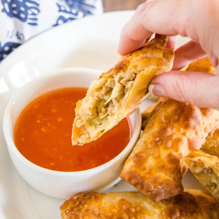 close up of cut egg roll being dipped in sauce