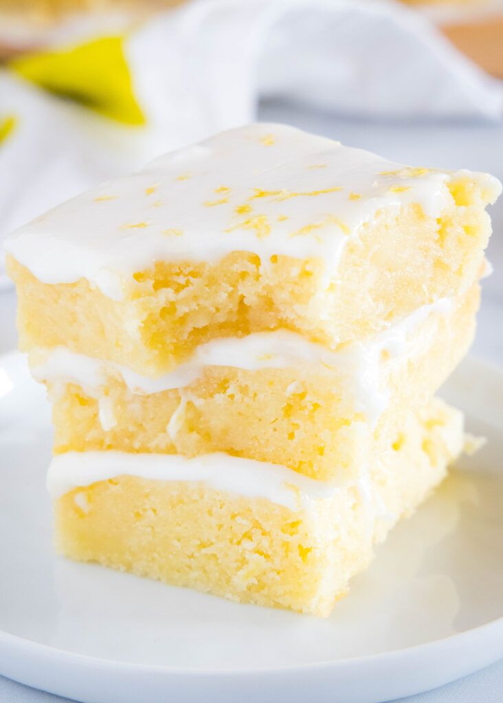 lemon brownies stacked on a plate with a bite taken out of the top one