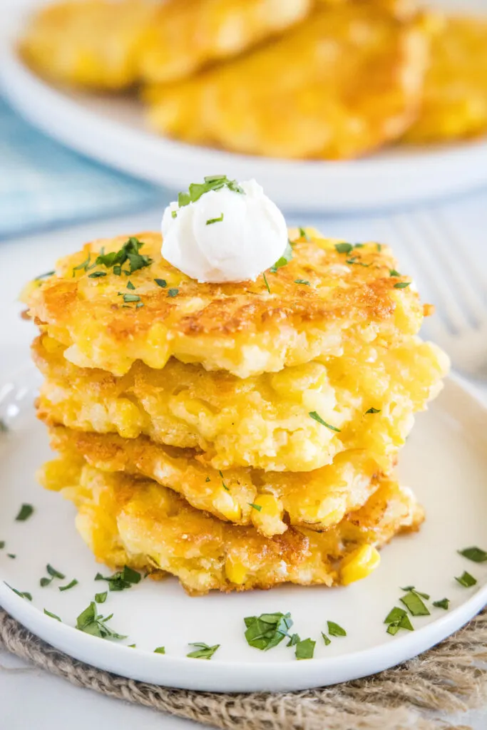 stack of corn fritters on a plate topped with sour cream