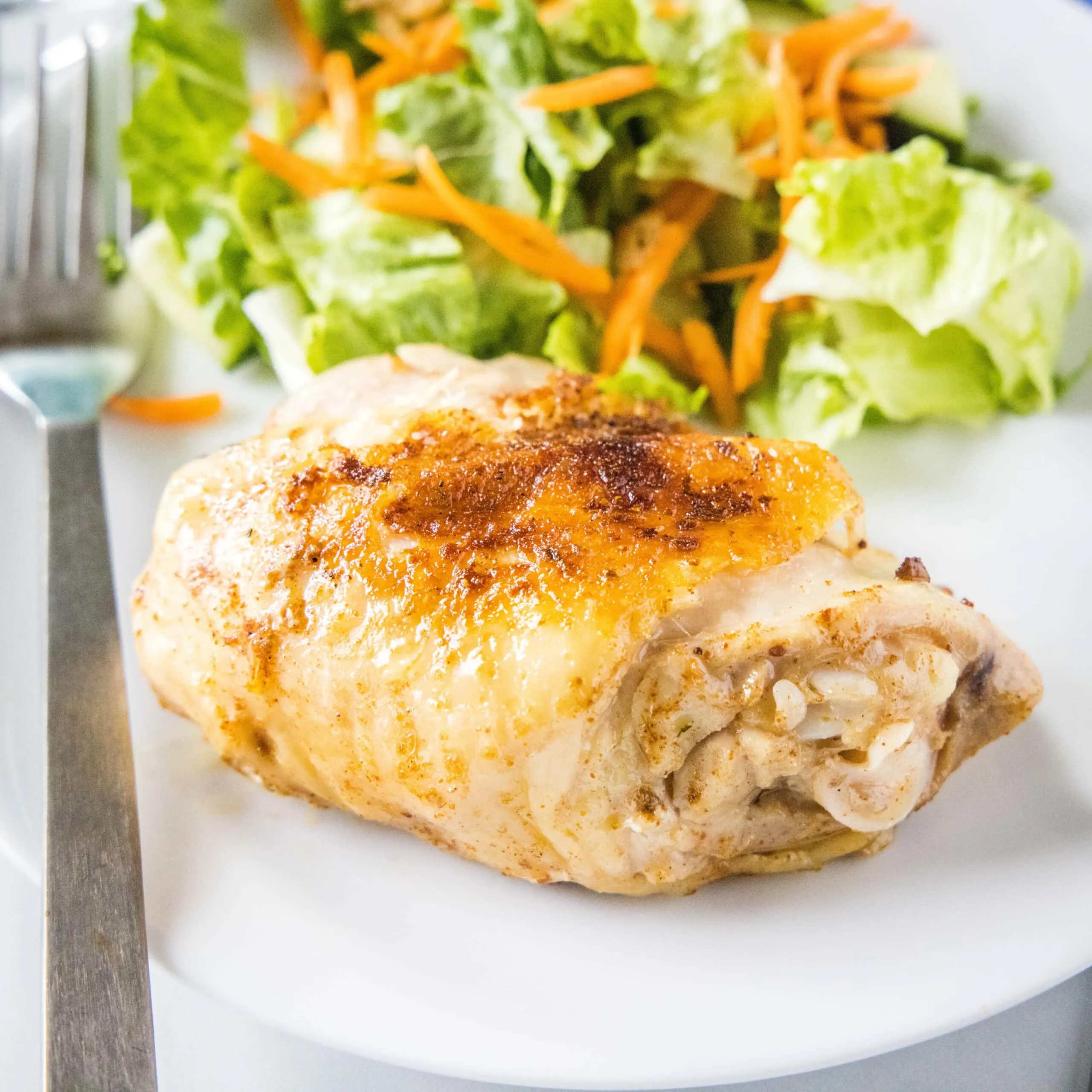 close up of cooked chicken thigh on a plate with salad
