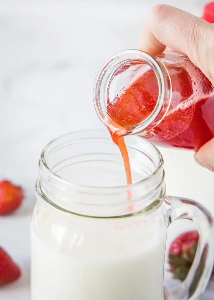 pouring strawberry syrup into cup of milk