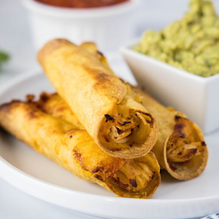 close up of crispy chicken taquitos on a plate with guacamole