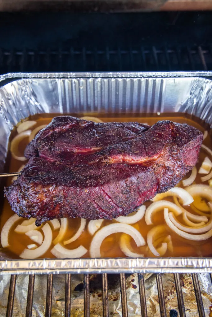 chuck roast in pan with onions and beef broth