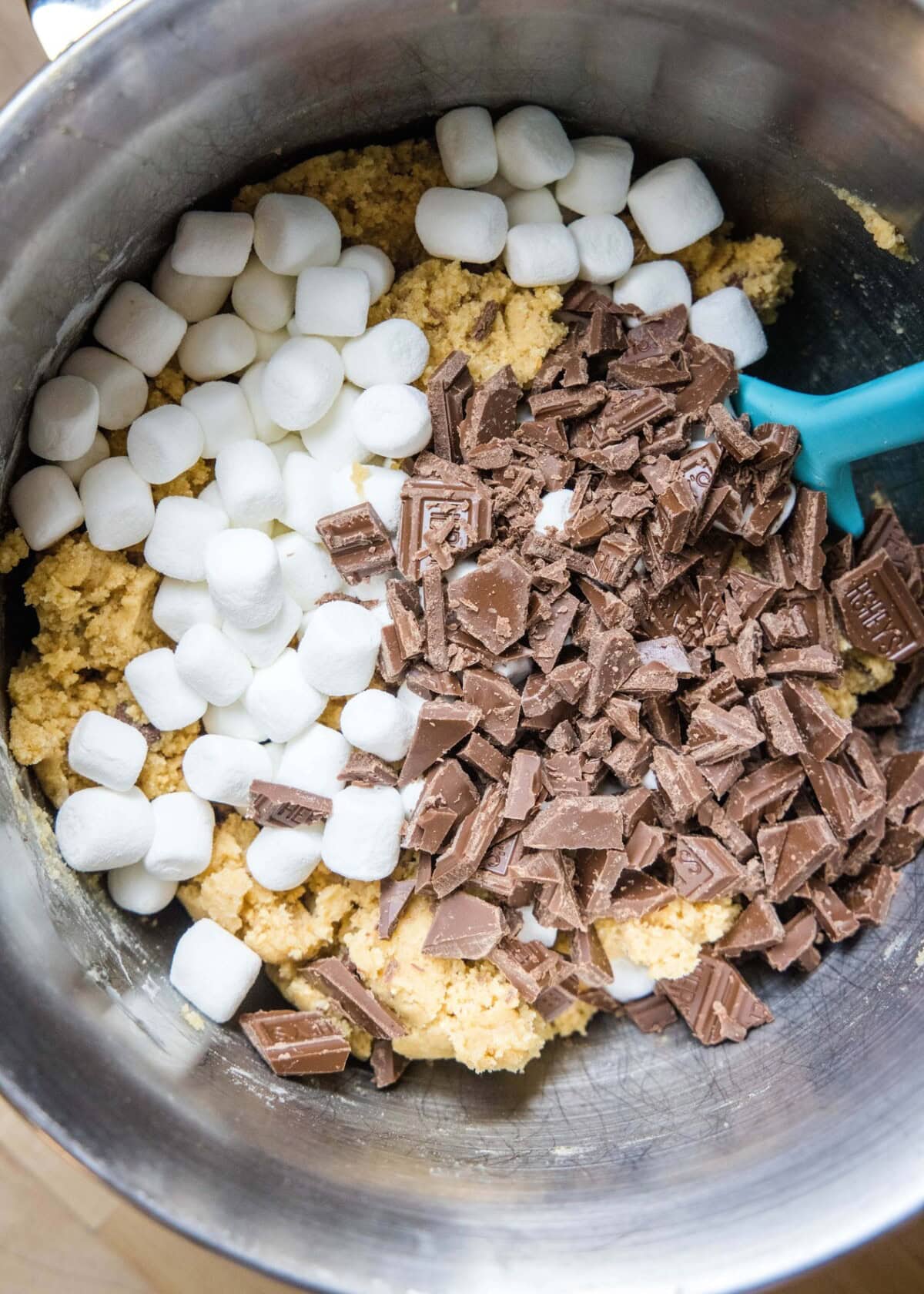 cookie dough in a mixing bowl with chocolate and marshmallows on top