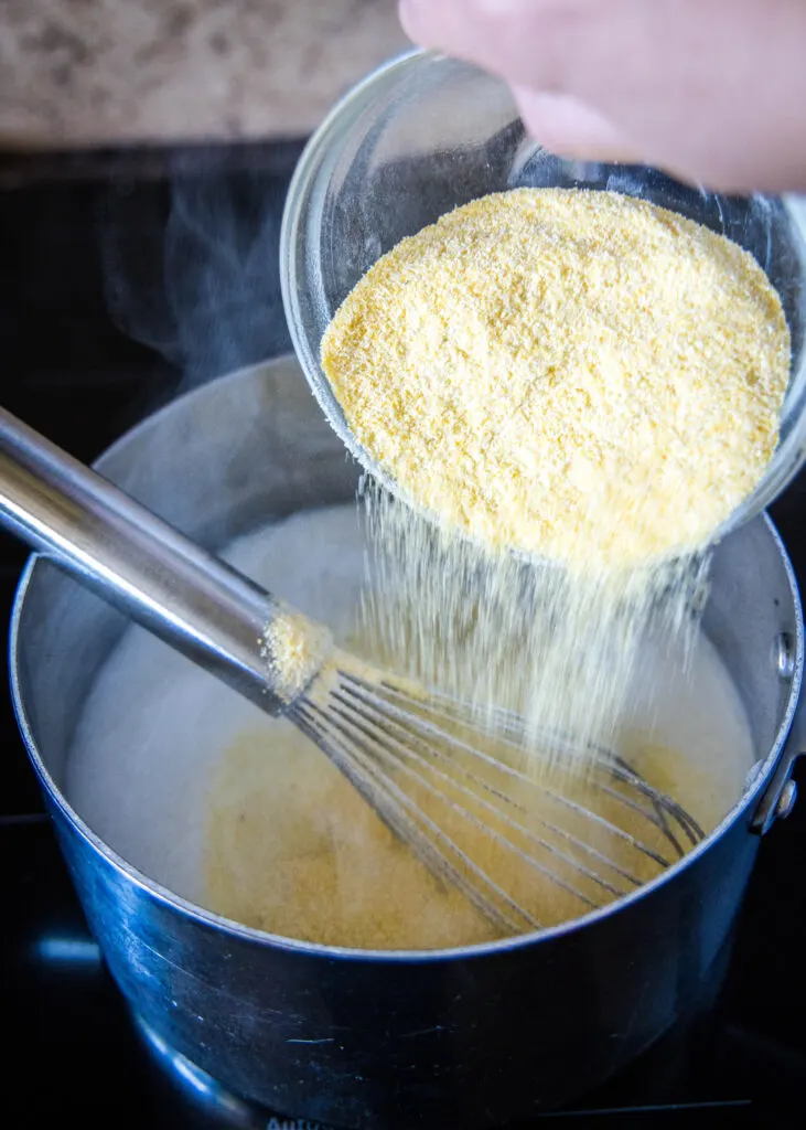 adding polenta to a pot of simmering milk