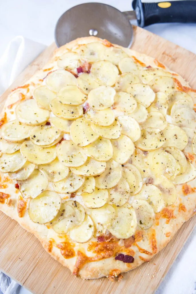potato pizza on a cutting board with pizza cutter