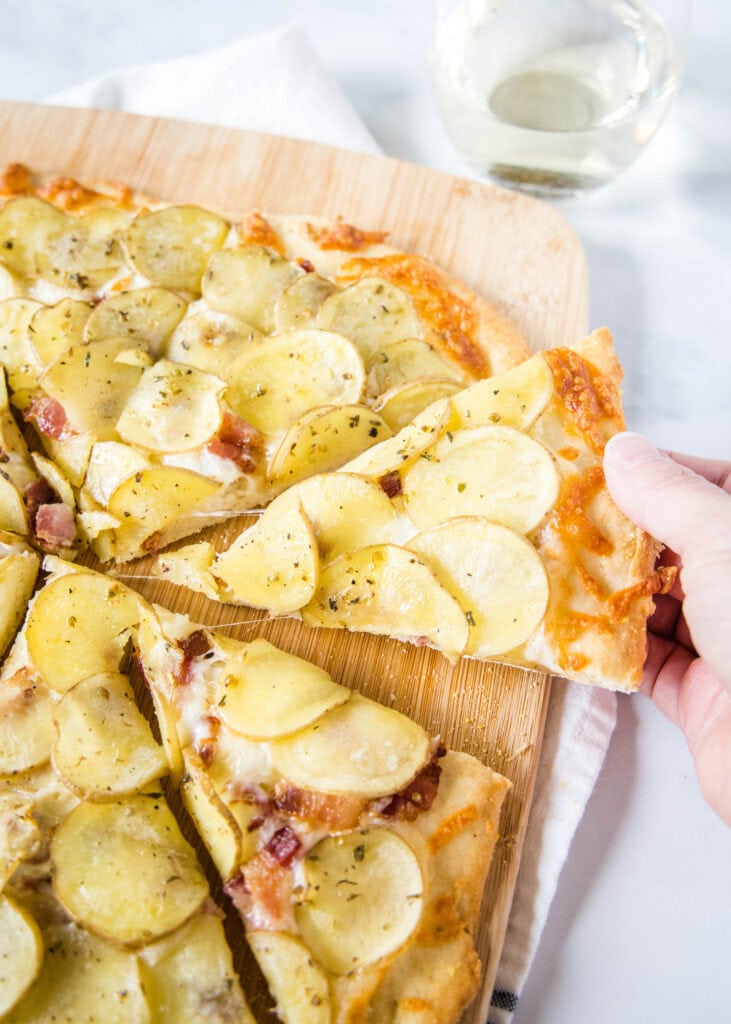 taking a slice of of potato pizza from a cutting board