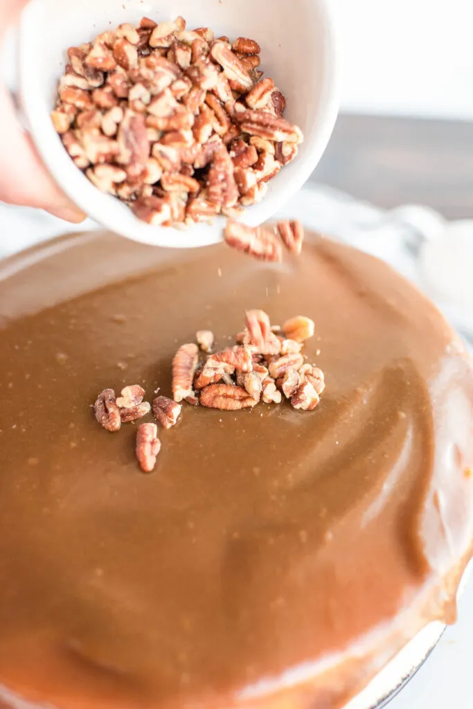sprinkling pecans over caramel on cheesecake