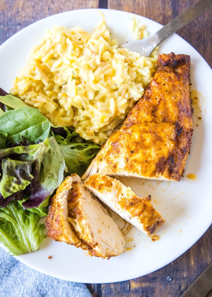 looking down on a plate of sliced chicken with salad and rice