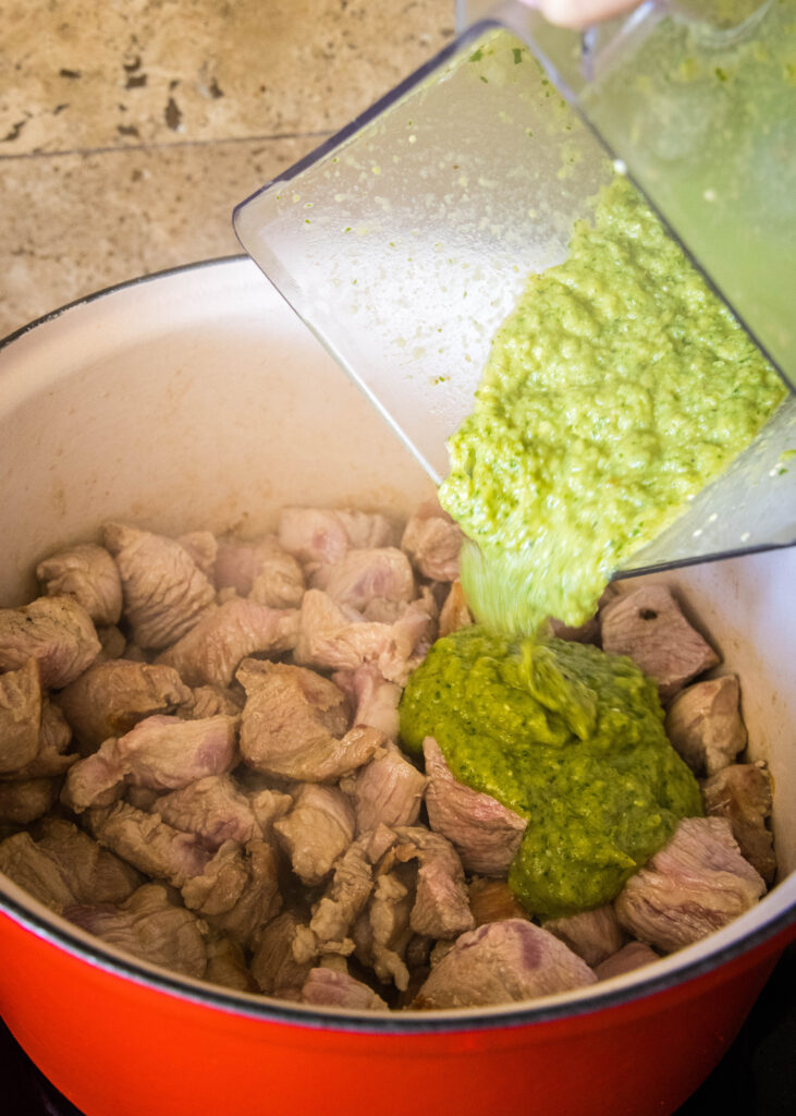 pouring green chili sauce into pot with browned pork