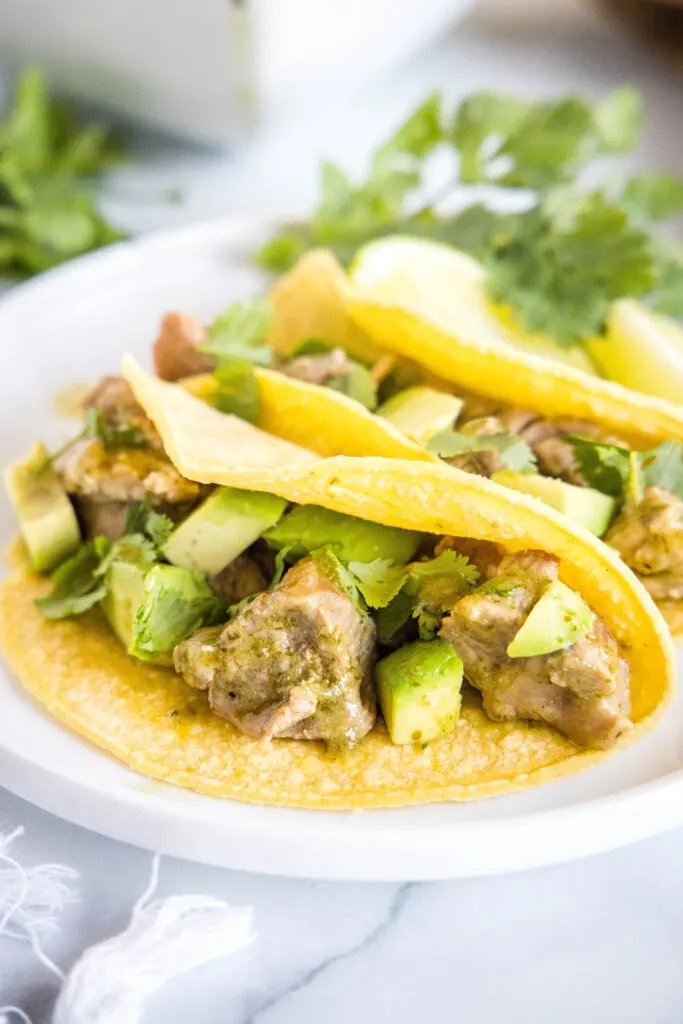 pork tacos topped with green chili on a white plate