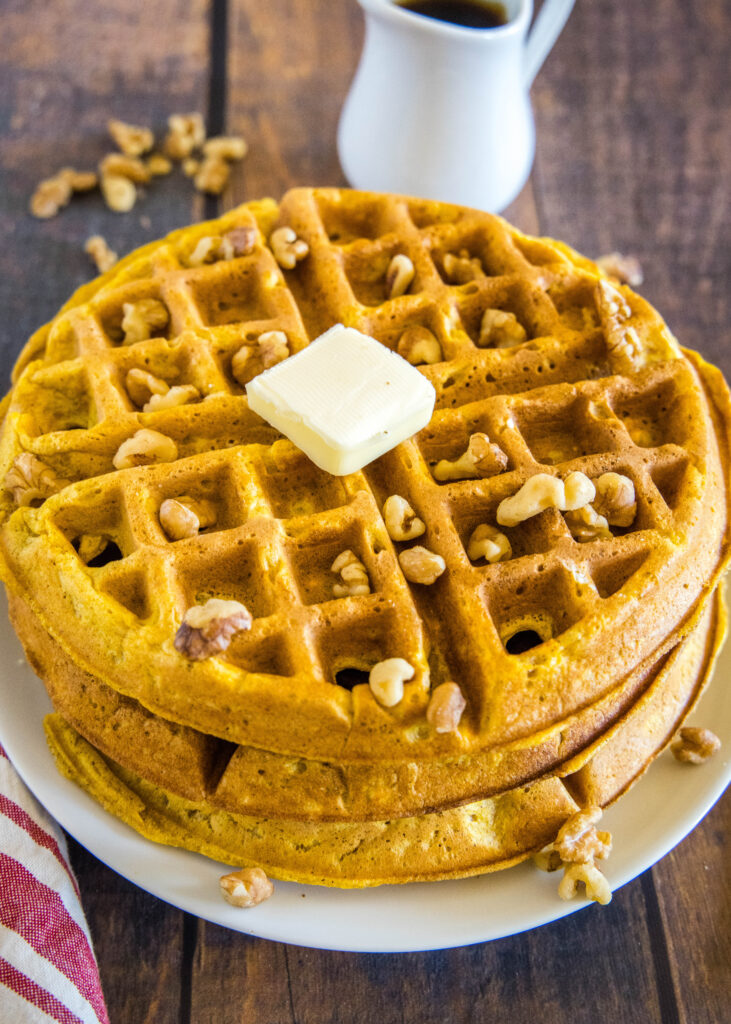 a stack of pumpkin waffles with pecans and butter on top