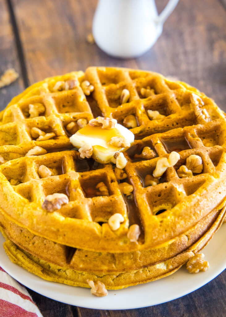 a stack of pumpkin waffles with syrup and walnuts