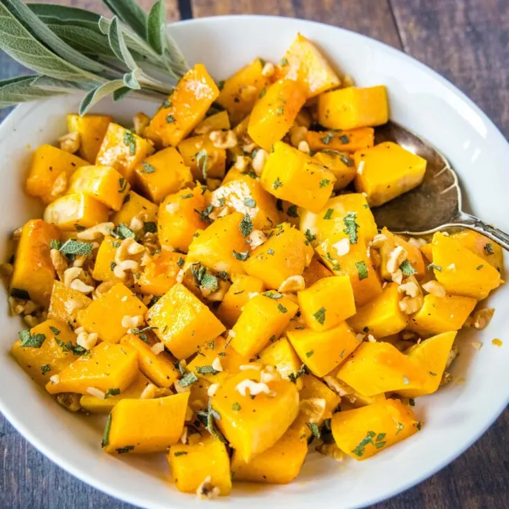 close up butternut squash in a bowl with a sprig of sage