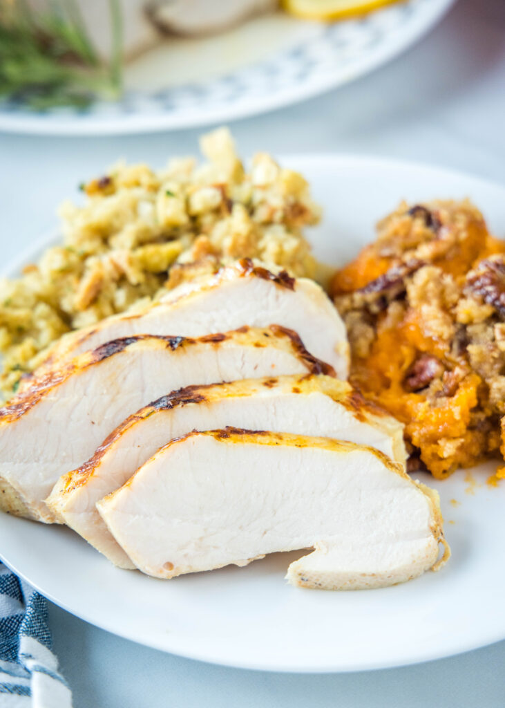 sliced turkey on a white plate with stuffing and sweet potatoes