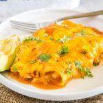 close up of 2 turkey enchiladas on a plate with avocado slices