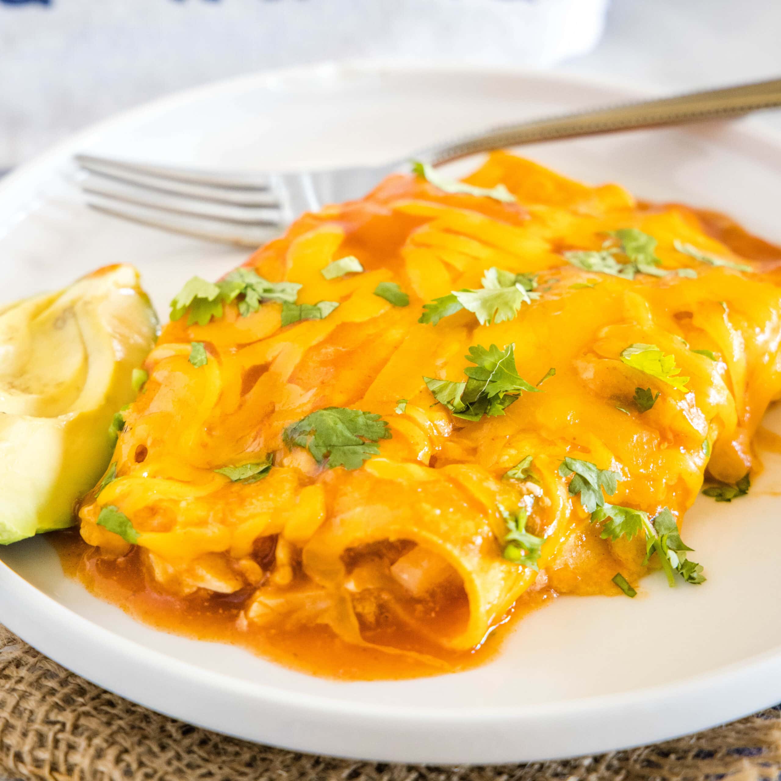 close up of 2 turkey enchiladas on a plate with avocado slices