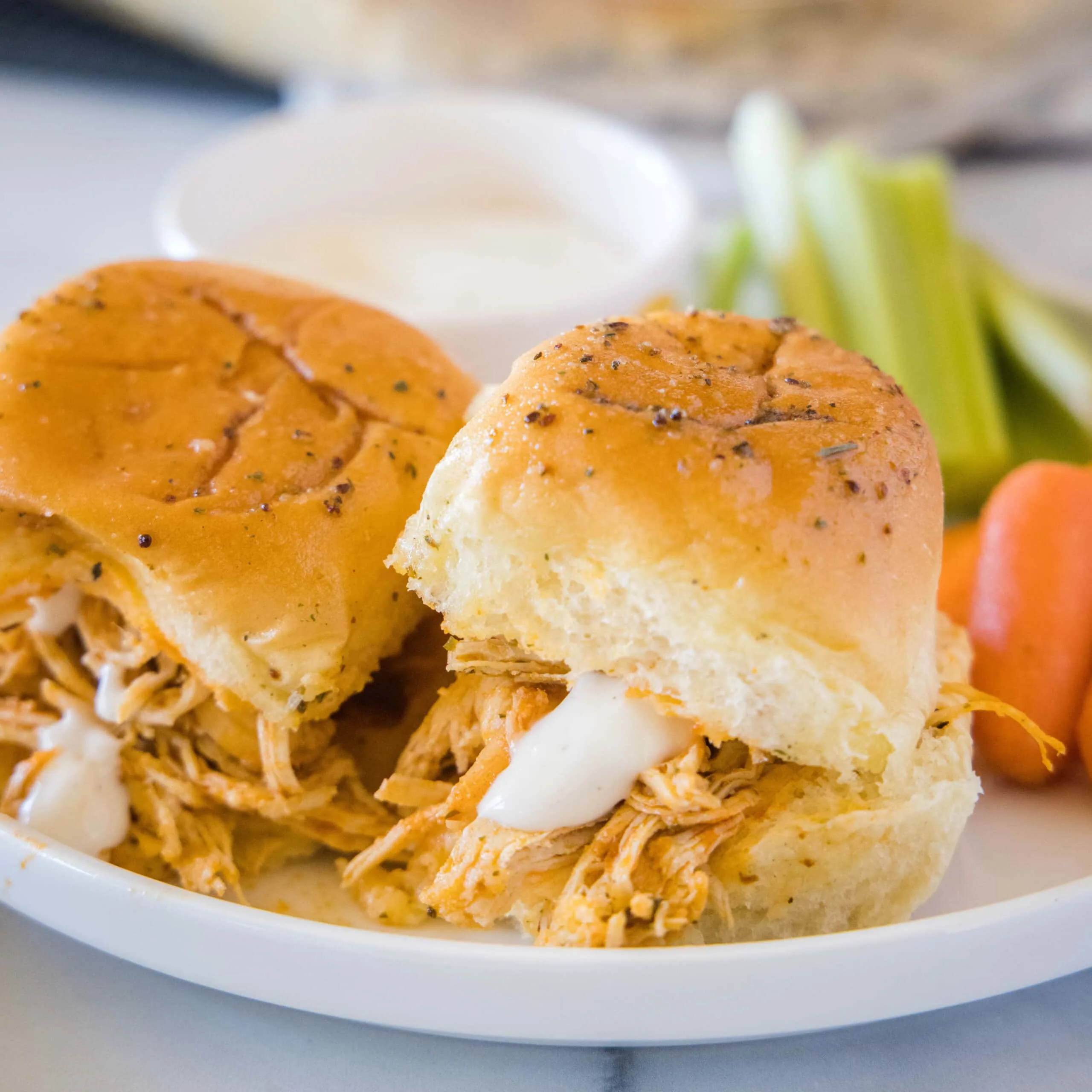 close up of buffalo chicken sliders on a white plate with ranch dressing