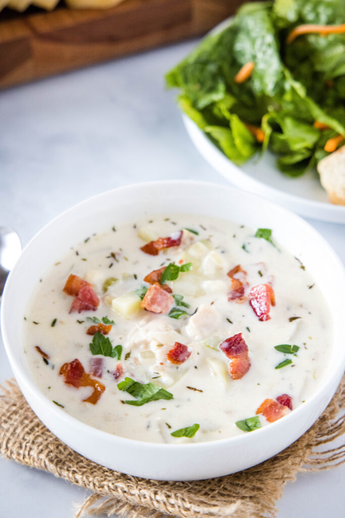a white bowl of clam chowder with bacon on top