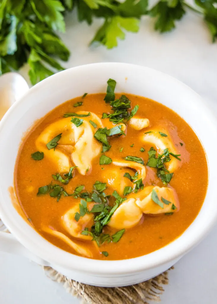 a white bowl filled with tomato soup and tortellini