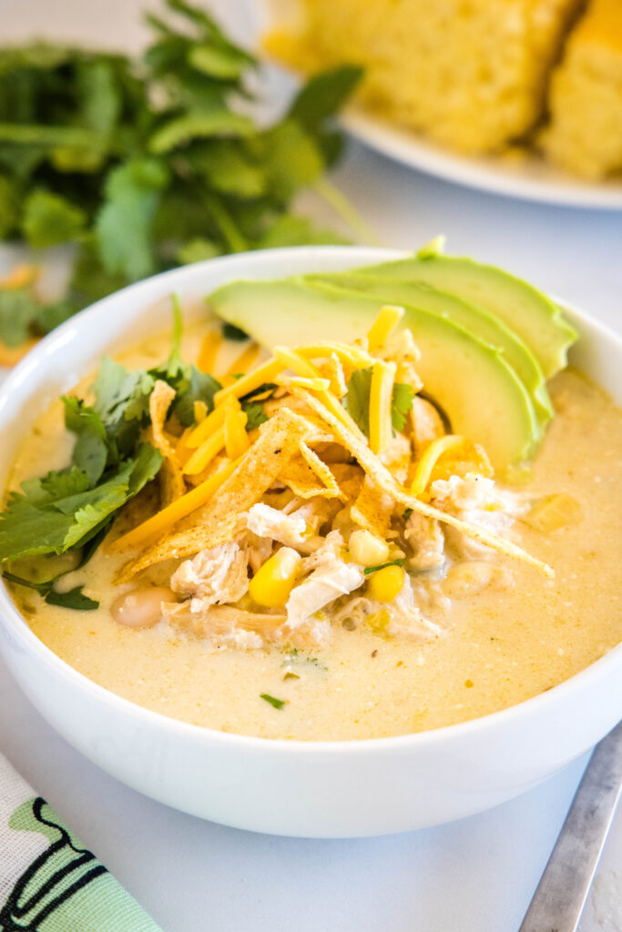 bowl of white chicken chili topped with tortilla strips, cilantro, cheese and avocado