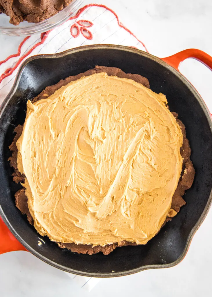chocolate cookie dough in a large skillet with a layer of peanut butter spread on top