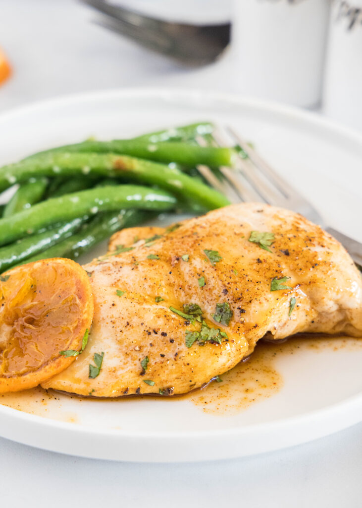 a white plate with orange glazed chicken and green beans